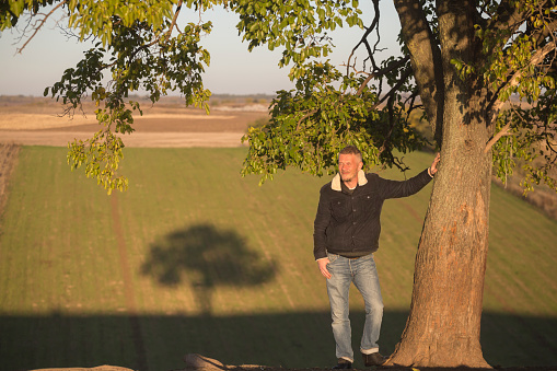 Adult man on the top of the hill leaning on tree