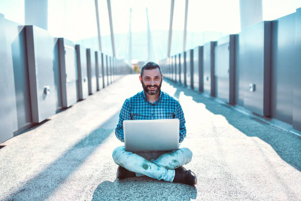 Smiling Latin Male Working On Laptop While Relaxing On Bridge