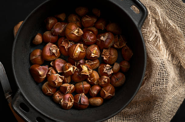 istock Fried cracked chestnuts in a frying pan on a black background and burlap, top view. Fresh roasted chestnuts for Christmas or holidays, seasonal dish 1283736468