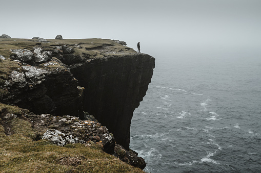 Lonely tourist on a hike along the cliffs of Eshaness, cold autumn day, Shetland Islands.