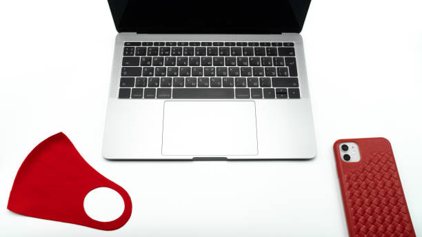 Red protective mask and phone in a red case lie next to the laptop, close up view. Concept of network communications, online shopping or laboratory work. Coronavirus compliance with safety standards about pandemic COVID-19. Self-isolation and social distance máscara protectora roja y teléfono en una caja roja se encuentran al lado de la computadora portátil, vista de cerca. concepto de comunicaciones en red, compras online o trabajo de laboratorio. covid-19. autoaislamiento y distancia social