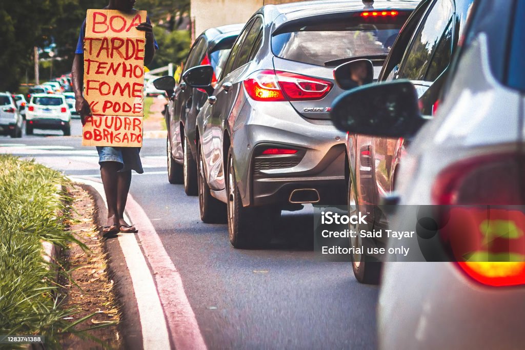 A homeless man asking for help Ribeirao Preto, SP, Brazil - March 2020: A homeless man in traffic with a cardboard sign asking for help. The sign says in portuguese âGood afternoon, I'm hungry. Can you help? Thanksâ Poverty Stock Photo