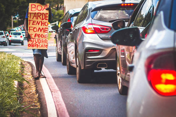 A homeless man asking for help Ribeirao Preto, SP, Brazil - March 2020: A homeless man in traffic with a cardboard sign asking for help. The sign says in portuguese âGood afternoon, I'm hungry. Can you help? Thanksâ poverty stock pictures, royalty-free photos & images