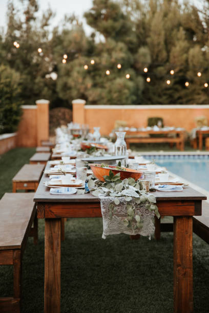 istock Backyard wedding setting - wooden tables with bohemian decor around swimming pool. 1283744614