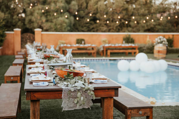 Backyard wedding setting - wooden tables with bohemian decor around swimming pool.