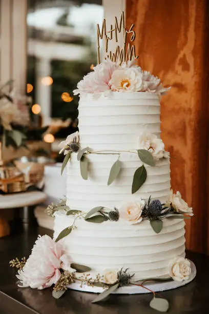 Three tiered wedding cake with eucalypus leaves and pink peonies, contemporary style