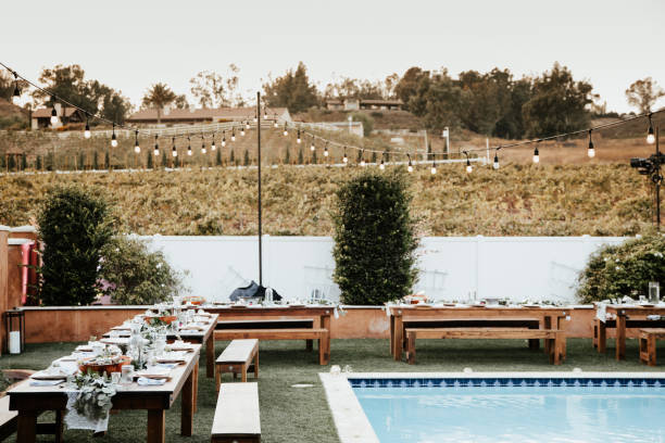 istock Backyard wedding setting - wooden tables with bohemian decor around swimming pool. 1283745399