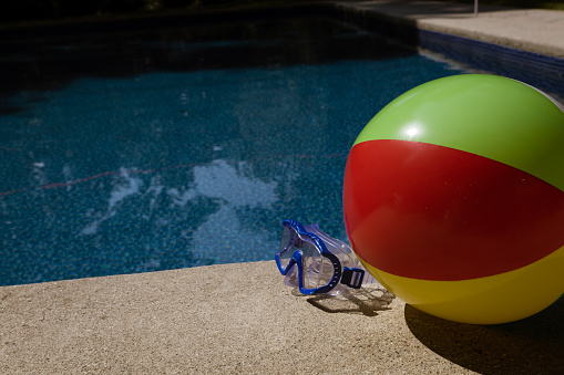 Water goggles and beach ball on concrete next to swimming pool