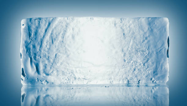 The rectangular block of pure transparent ice in cold blue tones on a mirroring surface with reflection.
