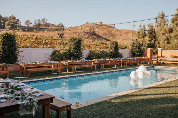 istock Backyard wedding setting - wooden tables with bohemian decor around swimming pool. 1283745979