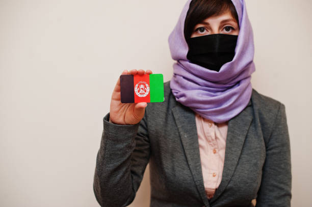 Coronavirus country concept. Portrait of young muslim woman wearing formal wear, protect face mask and hijab head scarf, hold Afghanistan flag card against isolated background. Coronavirus country concept. modest clothing stock pictures, royalty-free photos & images