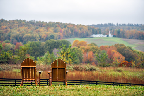 istock Sillas de madera vacías en otoño otoño temporada de follaje campo en Charlottesville bodega viñedo en las montañas de la cresta azul de Virginia con el día nublado cielo 1283749682