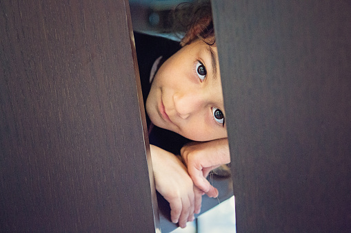 Portrait of little girl hiding under the table in her home