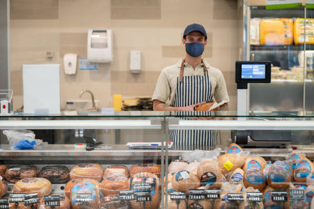 mann arbeitet an einem feinkostladen mit einer gesichtsmaske - supermarket meat store manager stock-fotos und bilder