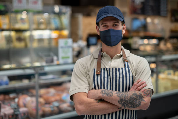mann, der während der pandemie in einer metzgerei arbeitet und eine gesichtsmaske trägt - supermarket meat store manager stock-fotos und bilder