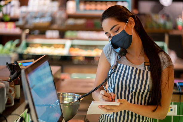 istock Waitress at a restaurant getting a delivery order on the phone and wearing a facemask 1283753339