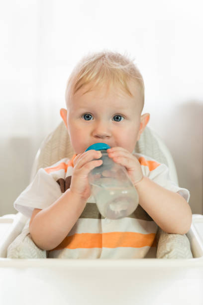istock A small white blue-eyed child sits at a table and drinks water from a bottle with pacifier. Independent 1283754800