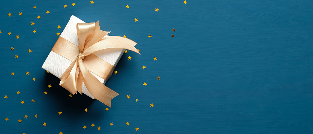 Caja de regalo blanca con lazo de cinta dorada sobre fondo azul con estrellas de confeti. Regalo de Navidad, sorpresa del día de San Valentín, concepto de cumpleaños. Plano, vista superior, espacio de copia. photo