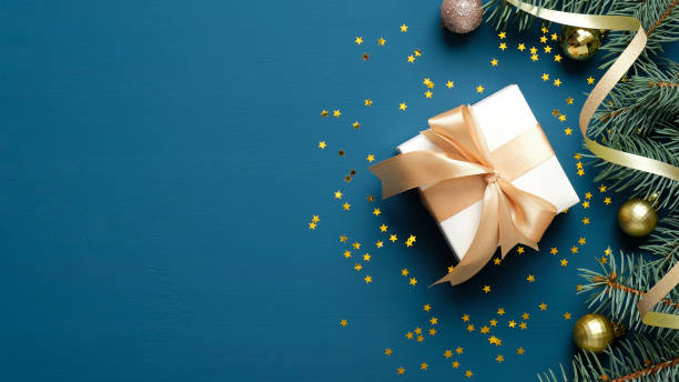 istock Christmas elegant composition. Blue Xmas background with white gift box, fir branches, balls, confetti. Christmas frame, greeting card template, banner mockup. Flat lay, top view, copy space 1283779471