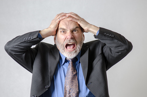 Business man holding head with two hands and screaming in studio with white background