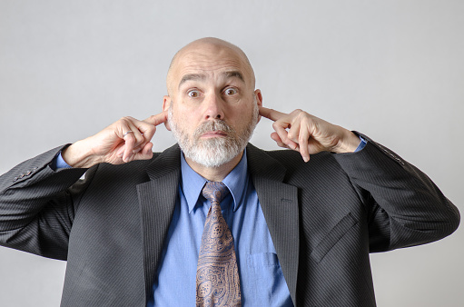 Business man with finger in his ears in studio with white background