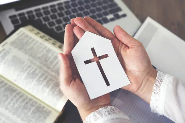 Woman holding paper church icon praying by faith with computer laptop, Church services online concept, Online church at home concept, spirituality and religion.