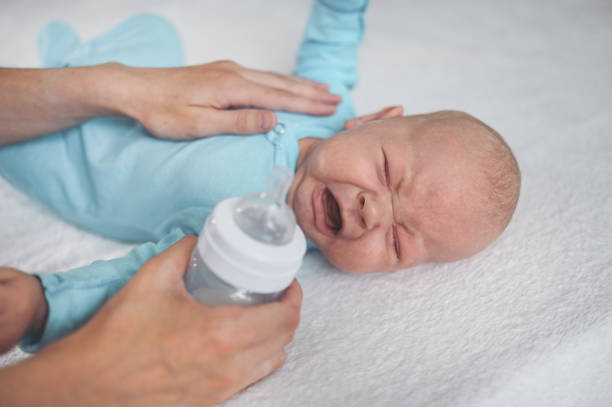 Cute emotional crying newborn infant boy laying on bed with milk bottle. Baby facial expressions. stock photo