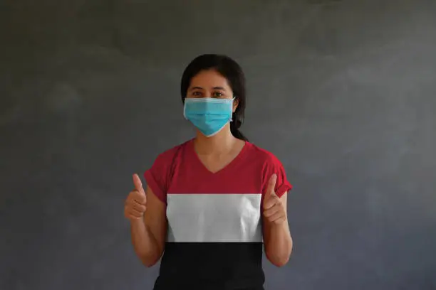 Photo of Woman wearing hygienic mask and wearing Yemen flag colored shirt with thumbs up with both hands