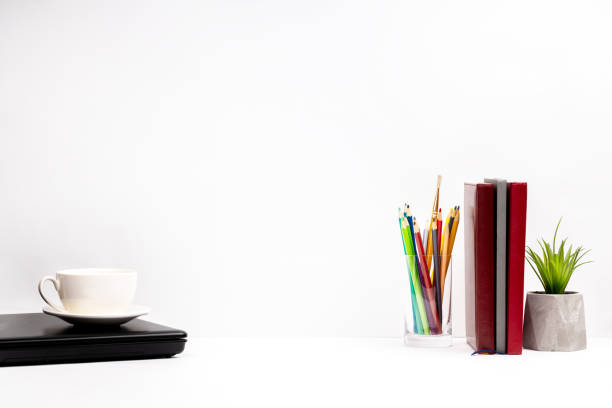 side view for a workplace. laptop and office supplies on white table top over grey wall background. rest time concept.