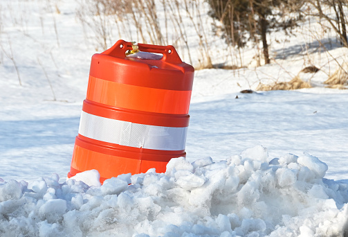 Orange and white construction barrel tipped over in snow drift.