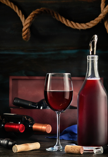 Low key image of red wine bottle and cup in a rustic nautical environment bar