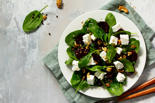 Vitamin snack. Salad with spinach, feta cheese, beetroot and walnut, vegetable oil sauceon a concrete table. Top view flat lay background. Copy space.