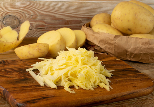 Raw grated potato on wooden cutting board background. Grate and sliced potatoes pile for swiss potato or pancakes on vintage chopping board closeup