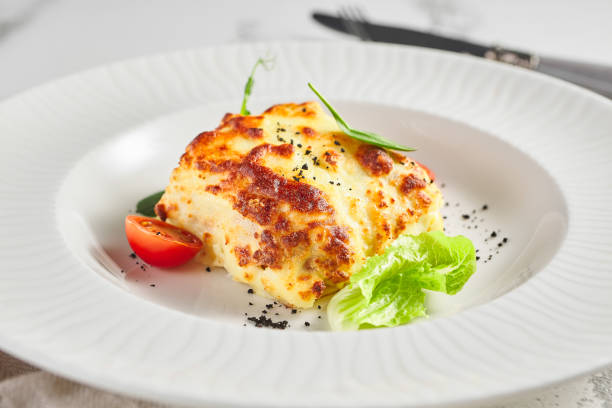 Lasagna with tomato and green leaf Lasagna with tomato and green leaf. Fish with bechamel sauce. White restaurant plate on light table seafood gratin stock pictures, royalty-free photos & images