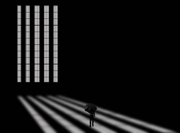istock Creative shot of a long window with rays of light coming through it and falling on the floor along with a male walking with an umbrella in his hand. Horizontal shot in black and white colors. 1283804577
