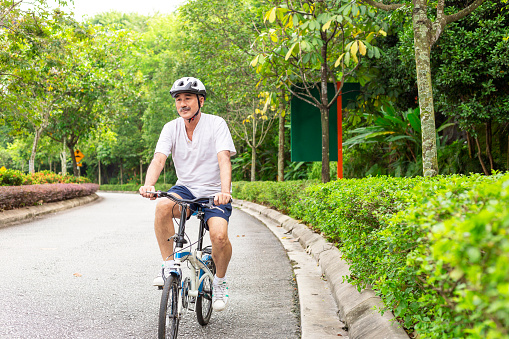 male cyclist with safety helmet riding a foldable bicyle in beautiful public park near a hill, as he padeling downhill