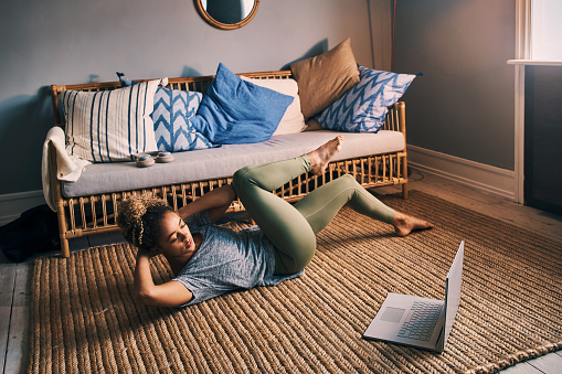 Shot of a sporty young woman using a laptop while exercising at home