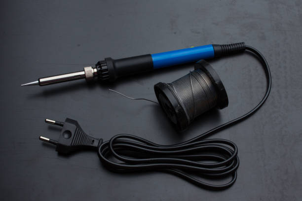 istock A soldering iron with a blue handle and a spool of solder on the old black desktop surface. Back light. 1283810114
