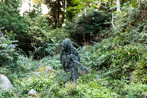 A soldier in a Ghillie suit camouflaged in the jungle.
