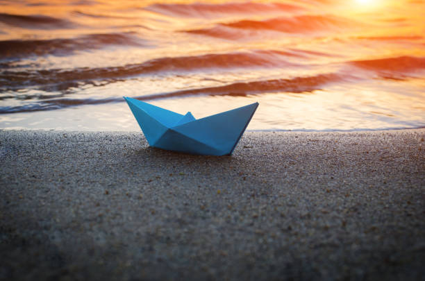 istock Lone blue paper boat washed up on the sandy beach at sunset. 1283815790