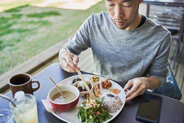 Japanese man eating a vegan lunch on the terrace of a vegan cafe. A Japanese man is sitting on the terrace of a vegan cafe. otsu city stock pictures, royalty-free photos & images