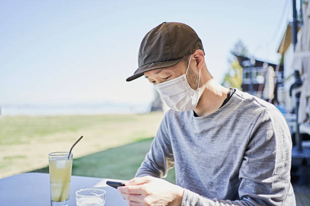 Man wearing a surgical mask uses a smartphone on the terrace of a cafe. The straws are stainless steel reusable straws. otsu city stock pictures, royalty-free photos & images