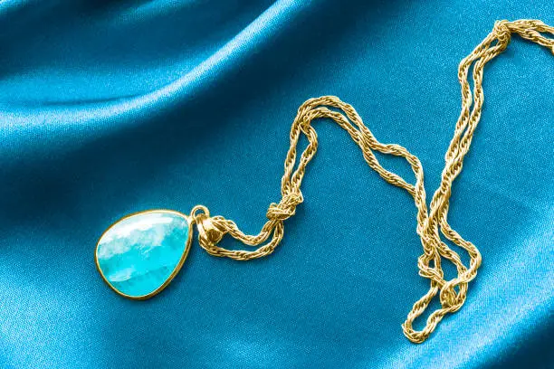 Elegant gold necklace with aquamarine pendant on blue satin background