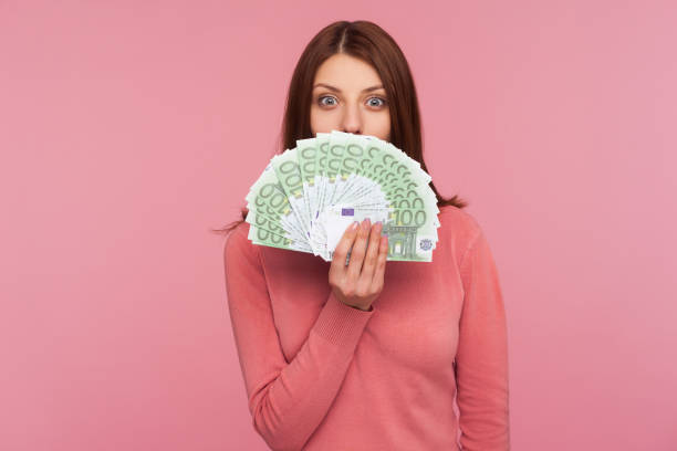 erstaunliche glückliche frau mit braunen haaren in rosa pullover versteckt gesicht hinter fan von euro-banknoten, zinslose bargeldabhebung - currency paper currency wealth human hand stock-fotos und bilder