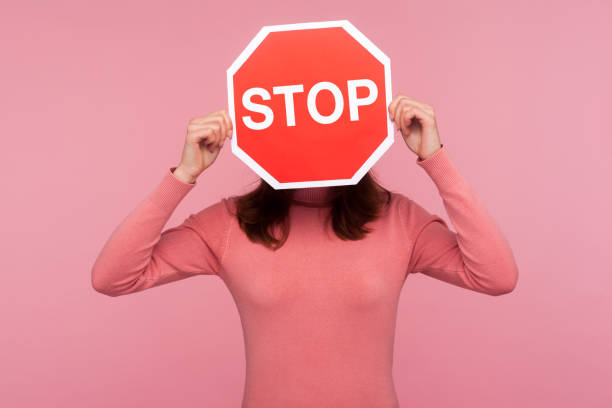 brunette woman in pink sweater hiding face behind stop sign, way prohibited, stop violence - aggression control clothing image type imagens e fotografias de stock