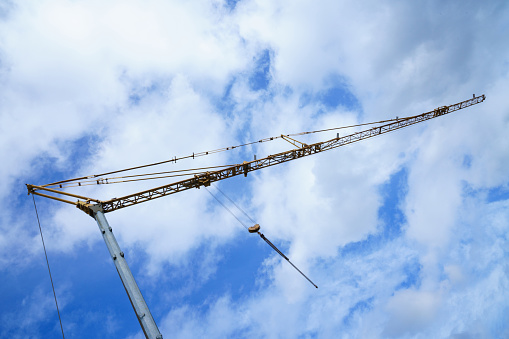 Boom of a construction crane against a blue sky with white clouds.