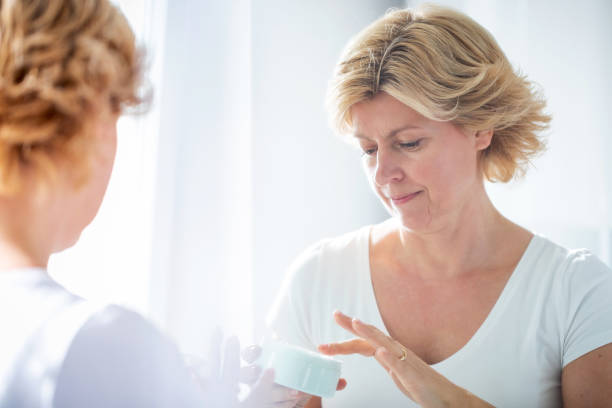 istock Blond woman's reflection in the mirror, taking face cream from jar with finger 1283828932