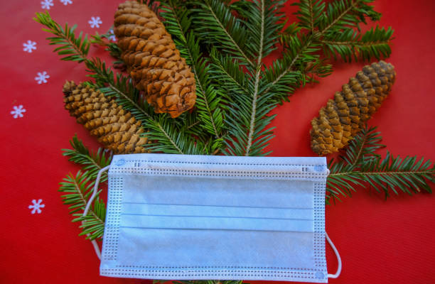 istock Fir tree with cones covered with medical face mask, white tinsel on red background close-up. Top view. Christmas, new year concept 1283830689