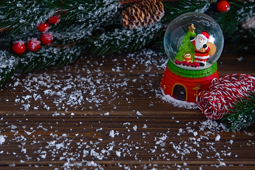 Snow-covered branches of a Christmas tree with cones and a Santa snow globe on a wooden background powdered with snow. Copy space.