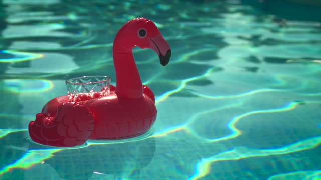 small inflatable flamingo cup holder floating in a pool with a glass in it in slowmotion